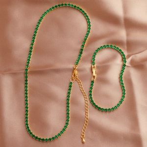 Close-up of emerald zircon necklace and bracelet set on elegant pink beige silk fabric