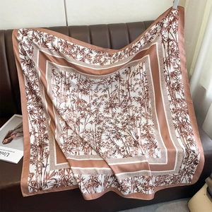 Detail of silk-like square scarf featuring brown bamboo leaf print on a leather sofa