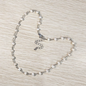 Detail of freshwater pearl necklace with silver chain shaped into a heart on wood background