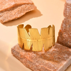 Macro shot of gold feather textured open cuff bracelet on a natural stone background