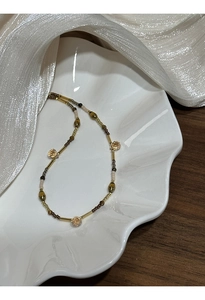 Detail of beaded necklace with gold tubes, tiger eye stones, and crystals in a ceramic dish