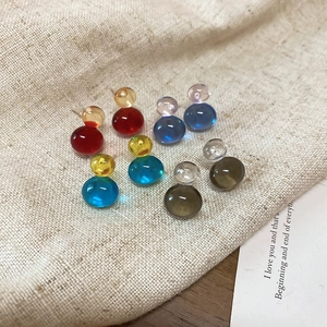 Top view of colorful glass double-ball stud earrings on beige linen fabric background