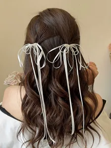 Detail of white silk bow hair clips with long tassels on wavy brown hair