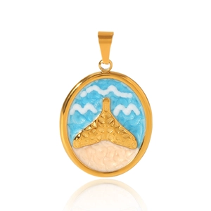 Detail of golden oval pendant with whale tail and blue enamel beach scene on white background