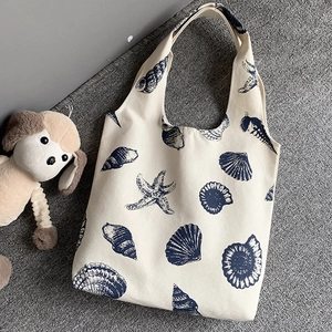 Close-up of canvas tote bag with navy starfish and seashell patterns on a grey carpet