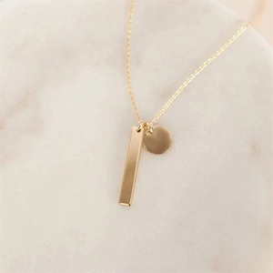 Détail macro du pendentif barre rectangulaire dorée et disque sur une chaîne fine