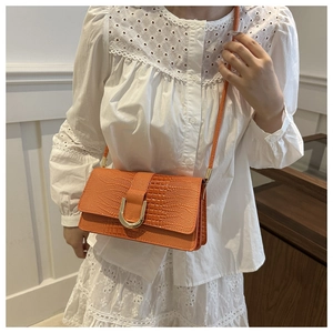 Sac à bandoulière orange motif crocodile avec boucle dorée en U sur une robe blanche