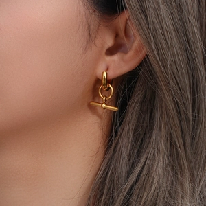 Detailed view of a golden hoop earring with a T-bar pendant on a fashion model