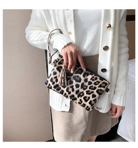 Chic leopard print envelope clutch bag with gold hardware held by a model in warm setting