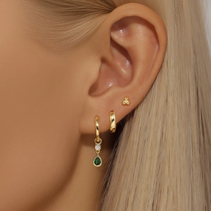 Close-up of gold hoop earrings set with green teardrop zircon and sparkling micro diamonds