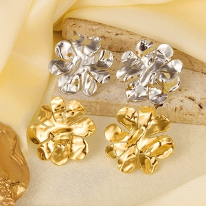Close-up of gold and silver flower stud earrings on textured stone and satin fabric