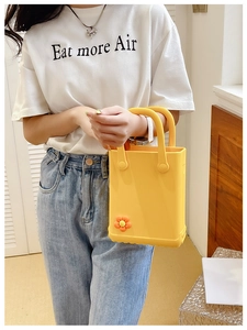 Detail der gelben EVA-Strandtasche mit dekorativen orangefarbenen Blumenanhängern