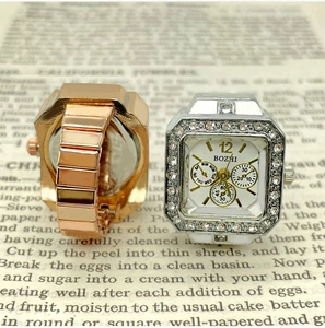 Detail view of square rhinestone-encrusted finger watches in rose gold and silver