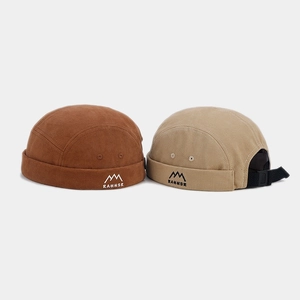 Détail de bonnets docker réglables en toile café et beige avec broderie de montagne