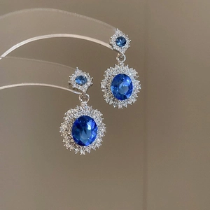 Close-up of elegant blue oval gemstone earrings with sparkling white diamond halo