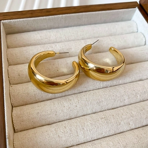 Macro detail of chunky gold C-shaped hoop earrings with polished mirror finish on linen