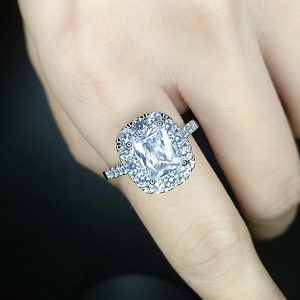 Close-up of silver halo ring with emerald-cut blue gemstone and side stones on finger