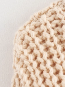 Close-up of beige chunky knit texture showing high-quality wool blend fabric detail