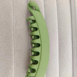 Vertical green matte banana hair clip for ponytails shown on grey textured background