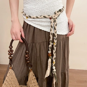 Detail of woven linen waist chain with resin beads paired with a rustic straw handbag