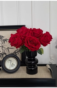 Velvet red roses in a black ceramic vase displayed on a tray against a white wall
