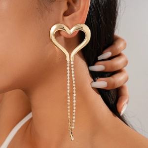 Close-up of golden hollow heart earrings with shimmering tassel chains on a model