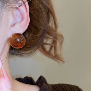Detailed close-up of a model wearing dark amber resin ball earrings with a glossy finish