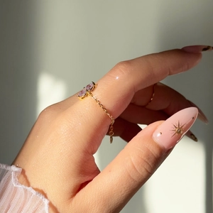 Detailed view of an adjustable gold chain ring featuring two pear-cut purple gemstones