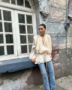 Detailed view of the pleated beige top with long sleeves and light blue denim flares