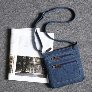 Detail view of blue denim crossbody bag featuring triple front zipper pockets and retro style