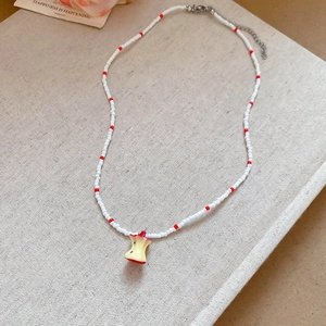Détail du collier de perles avec perles rouges et blanches et pendentif trognon de pomme