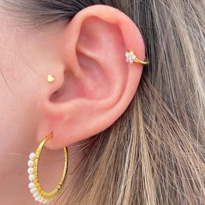 Detail of gold heart stud, zircon ear cuff, and pearl hoop earring set on model