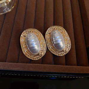 Macro detail of vintage gold oval earrings with textured texture and white pearl inlay