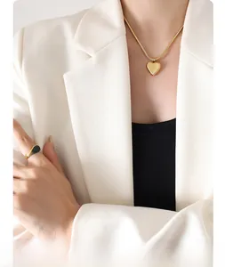 Detail of gold snake chain with heart pendant and emerald green gemstone ring on a model