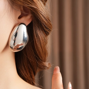 Close-up of minimalist silver teardrop earring worn by a model in soft lighting