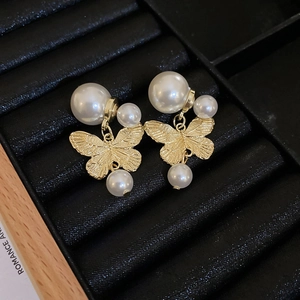 Detail of golden butterfly earrings with faux pearls on a black jewelry tray