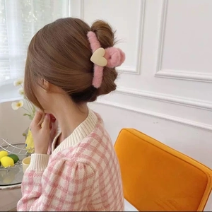 Pink plush hair claw clip with cream heart detail worn by model on a bun hairstyle