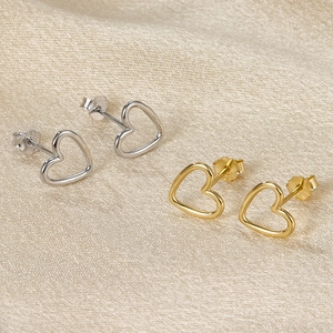 Detailed view of silver and gold S925 sterling silver heart studs on beige fabric