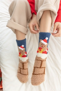 Close-up of thick coral fleece Christmas socks with bear and hat patterns on a bed