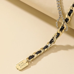 Dettaglio collana dorata intrecciata con nastro nero, cristalli e pendente Good Luck