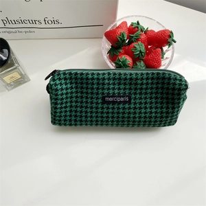 Green houndstooth plaid pencil case with zipper and merciparis label on a desk