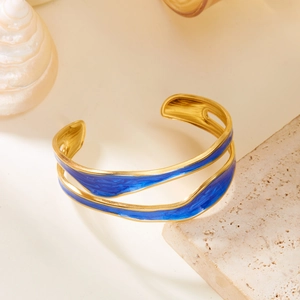 Close-up of golden irregular wavy cuff bracelet with deep blue enamel inlay and open design