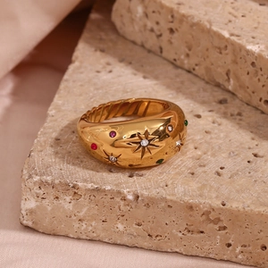 Detail of 18K gold star ring with colorful stones on beige stone, close-up macro view