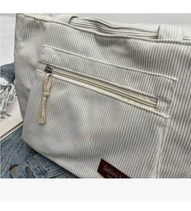 Detail of cream corduroy tote bag showing ribbed texture, zip pocket, and leather patch
