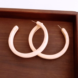 Detailed close-up of beige resin C-shape hoop earrings with marble texture on wood
