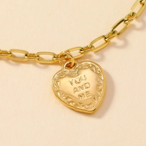 Close-up of gold chain bracelet with engraved You and Me heart pendant detail