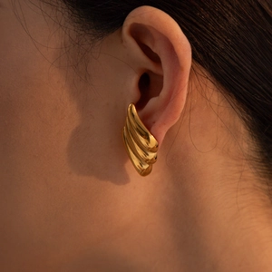 Close-up of elegant gold wave stud earring in stainless steel worn by a model