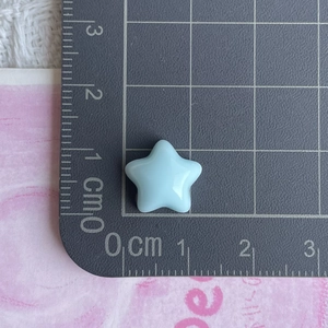 Close-up of a mini light blue resin star charm measuring 1.2cm on a measuring ruler
