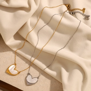Detail of 18K gold and silver heart necklaces with white shell inlay on beige fabric