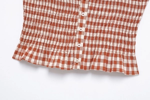 Detail of orange checkered smocked top with white buttons and ruffled hemline